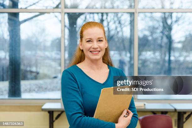 schöne reife professorin lächelt in die kamera, während sie ihr klemmbrett hält - gemeindezentrum stock-fotos und bilder