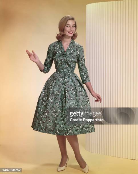 Posed studio portrait of a female fashion model wearing a grey-green floral patterned summer dress with a cinched in belted waist, full skirt and tie...