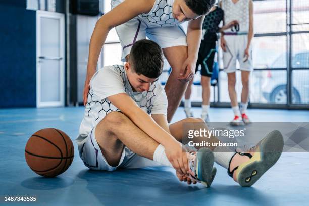 teenage boy injuring his ankle while playing basketball indoors - sports injuries stock pictures, royalty-free photos & images