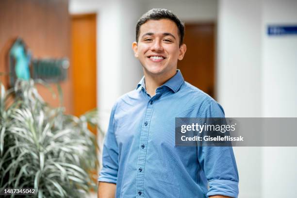 jovem empresário sorridente parado no corredor de um escritório - só um homem jovem - fotografias e filmes do acervo