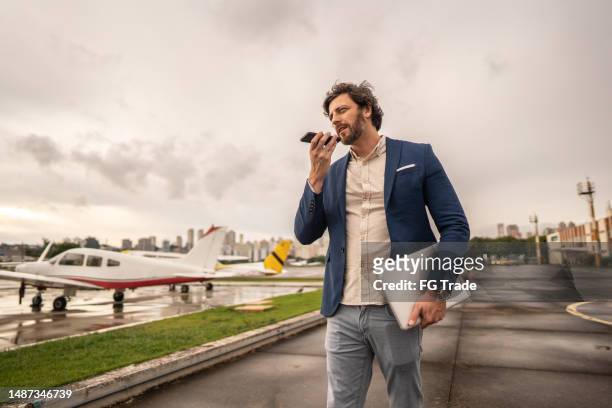 mid adult businessman sends a voice message while walking in a airport hangar - dictaphone stock pictures, royalty-free photos & images