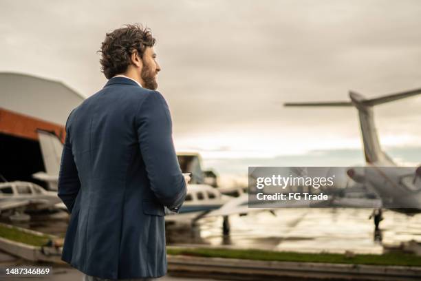 mid adult man looking away contemplating in the airport hangar - high society stock pictures, royalty-free photos & images