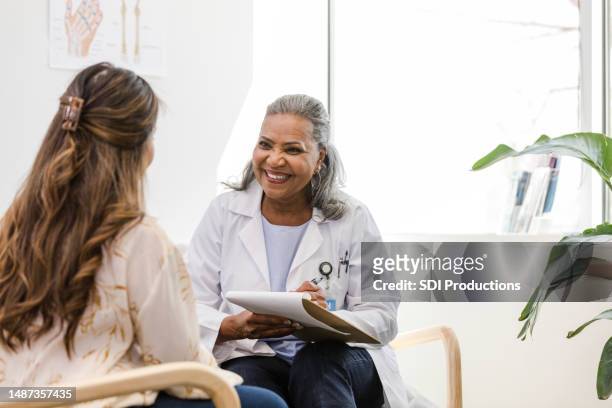 alegre profesional de la salud madura sonríe mientras le da a su paciente los resultados de la prueba - assistente social fotografías e imágenes de stock
