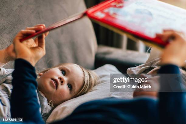 mother and daughter reading book on a sofa. - erzählen stock-fotos und bilder