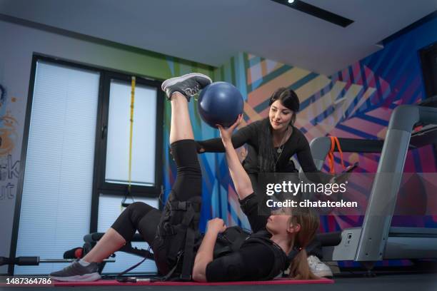 beautiful blonde in an electric muscular suit for stimulation makes an exercise on the rug - personalized medicine stock pictures, royalty-free photos & images