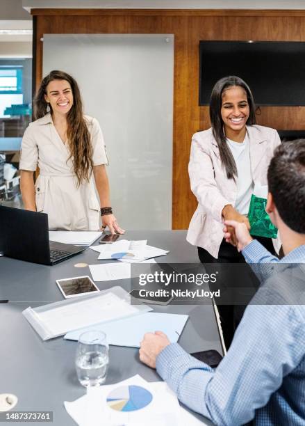 woman holding a present shaking hands with a colleague  during meeting in office boardroom - werk in uitvoering stockfoto's en -beelden