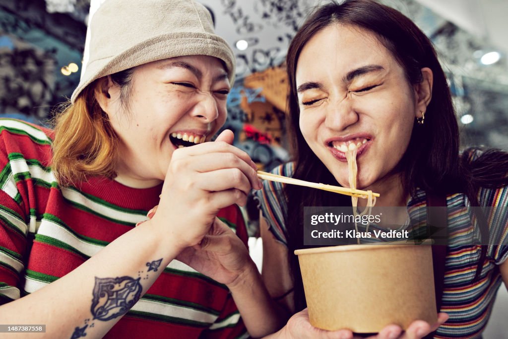 Woman feeding noodles with chopsticks to friend