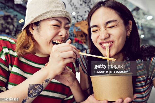 woman feeding noodles with chopsticks to friend - woman eat noodles imagens e fotografias de stock