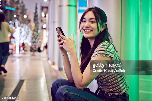 happy woman with smart phone sitting at street - bangkok nightlife stock pictures, royalty-free photos & images