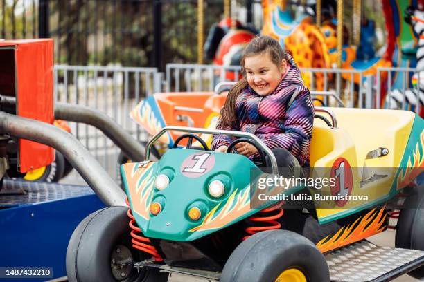 young girl grinning riding her bright colored toy car in amusement park - draaimolen stockfoto's en -beelden