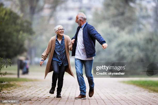 playful senior couple having fun while running in the park. - mature couple winter outdoors stock pictures, royalty-free photos & images