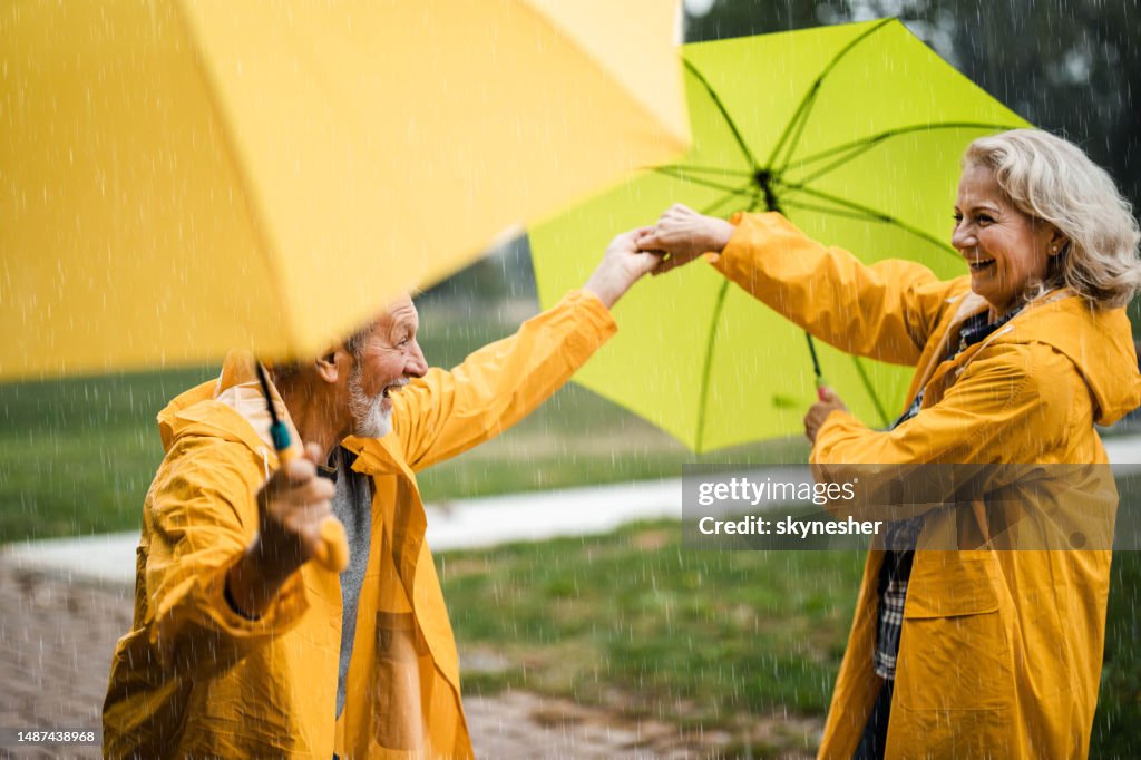 Happy mature couple in yellow raincoats having fun on rain in nature.