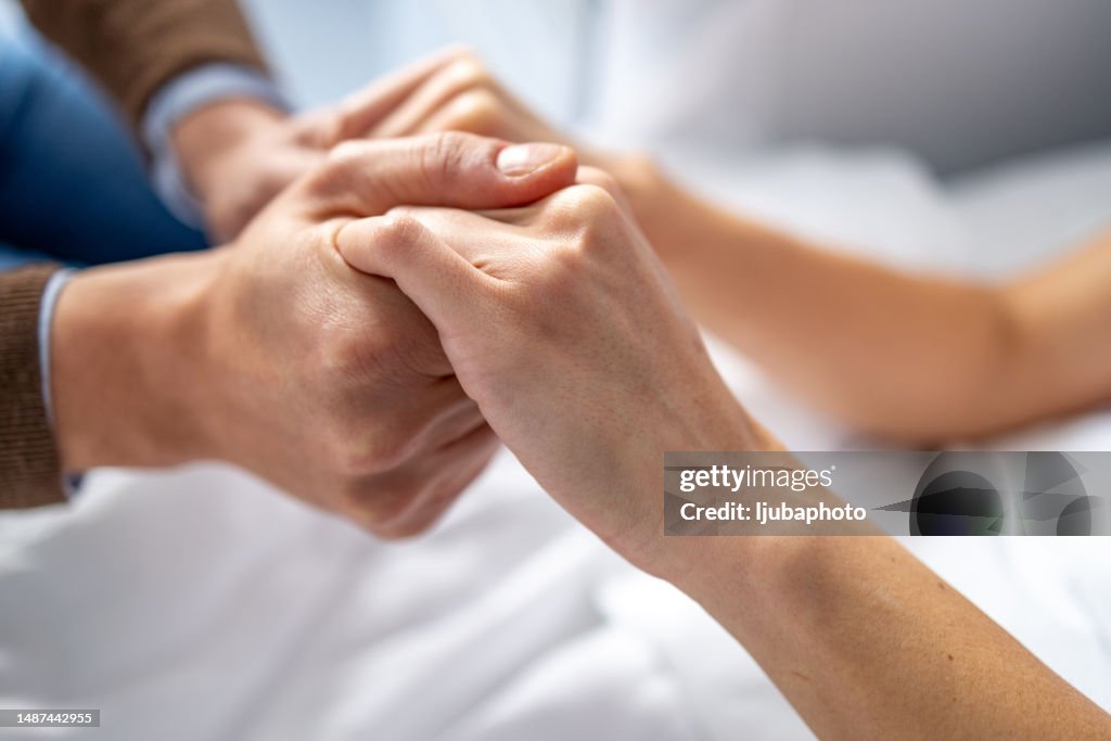 Man holding woman hand in hospital bed.