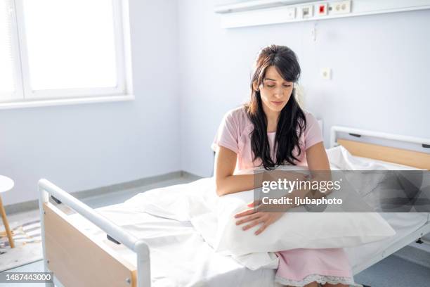 anxious, sad, young woman wearing hospital gown looks down - hospital gown imagens e fotografias de stock