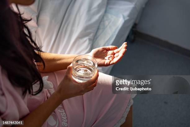 overhead view of a woman feeling sick, taking medicines in hand with a glass of water - white bed stockfoto's en -beelden