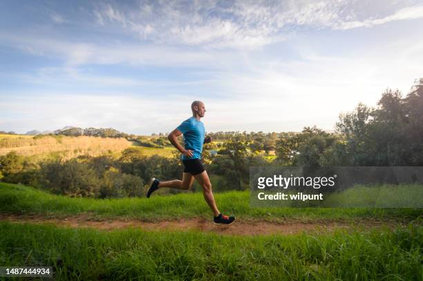 side view male trail runner long strides fast running in country side - long grass stockfoto's en -beelden