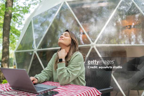 woman  sitting at table and using laptop in front of a geo dome glamping tent. - person with a neck pain stock pictures, royalty-free photos & images