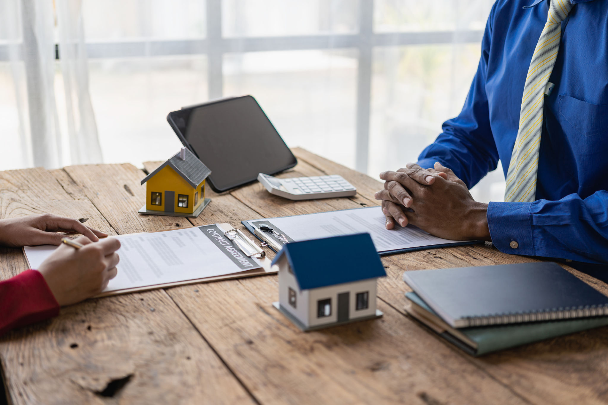 Real estate agents offer contracts to buy or rent housing. Businessman holding model small building house with property insurance at table in home sales office Real estate agents offer contracts to buy or rent housing. Businessman holding model small building house with property insurance at table in home sales office