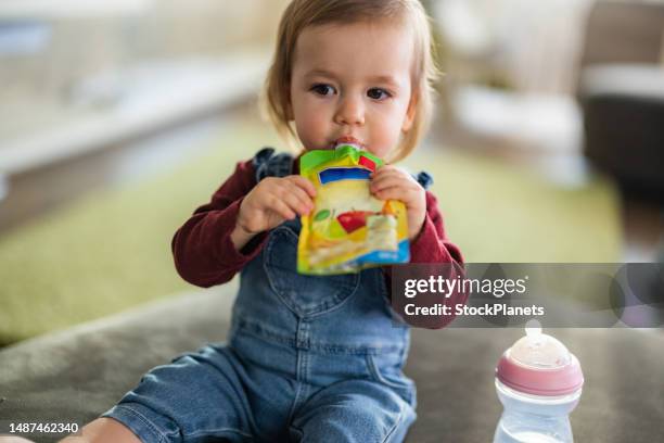 cute little girl eating fruit puree in pouch - baby food stock pictures, royalty-free photos & images