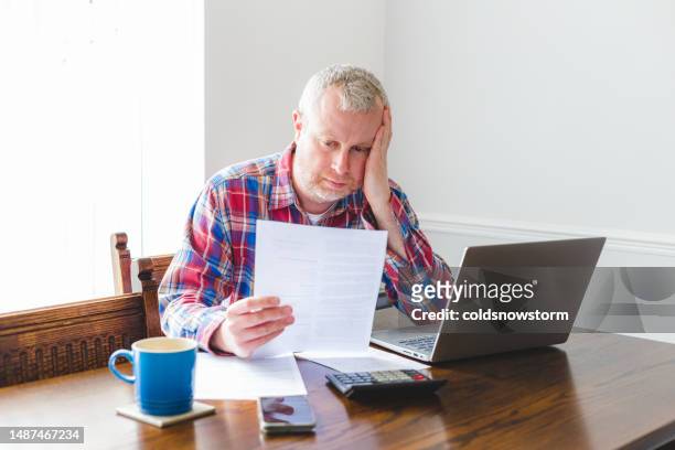 worried man checking energy bills at home - price calculator stockfoto's en -beelden