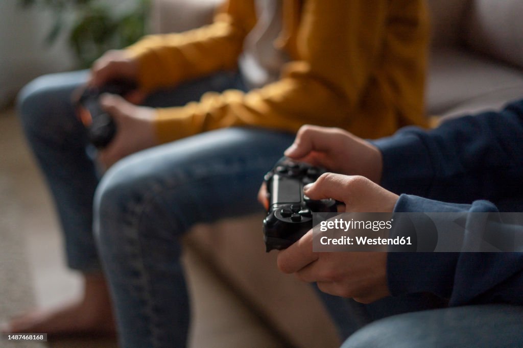 Hands of boys holding gaming consoles at home