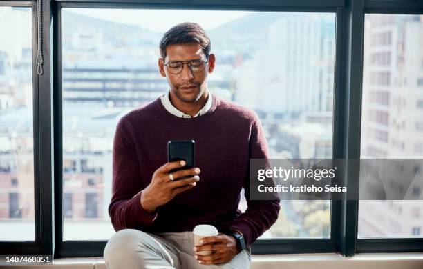 relax, coffee and business man with phone at a window on social media in office. smartphone, tea and indian male entrepreneur reading, searching and online for meme, networking or email on a break - meme text stock pictures, royalty-free photos & images