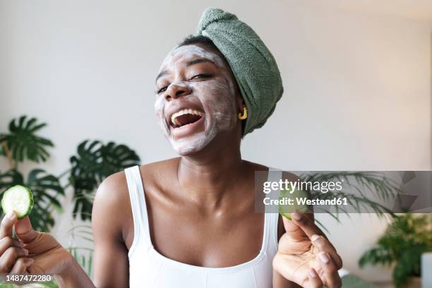 cheerful young woman holding slices of cucumber at home - cucumber eye mask stock pictures, royalty-free photos & images