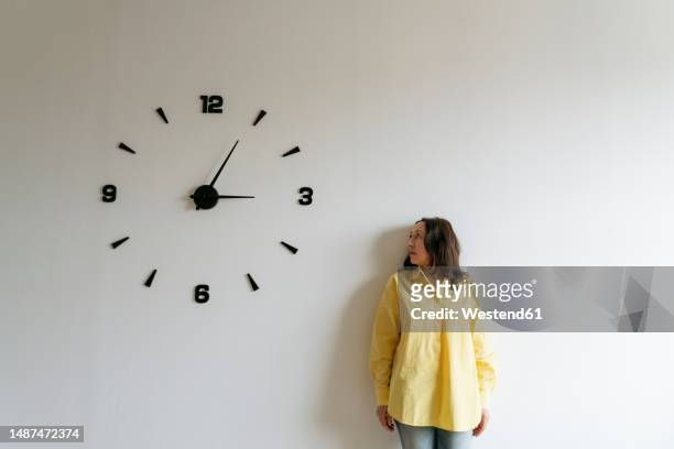 woman looking at large clock on white wall - wall clock stock pictures, royalty-free photos & images