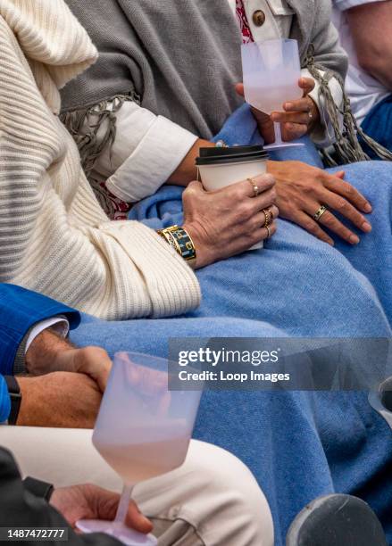 Women's hands are seen in close-up wearing jewellery while holding takeaway glasses and resting on blue blankets at the Queen's Club tennis...