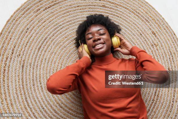 happy young woman with eyes closed wearing wireless headphones and lying on rug - beige carpet stock pictures, royalty-free photos & images