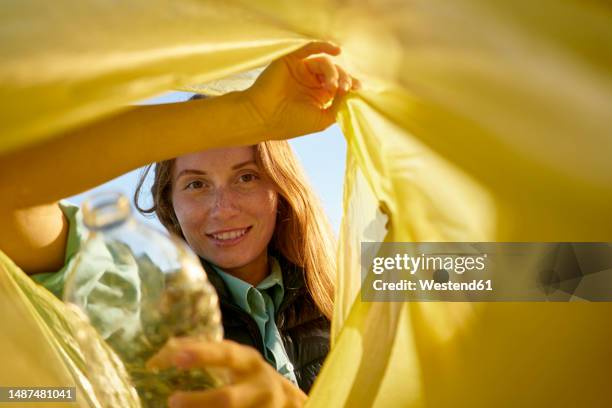 smiling woman looking inside yellow garbage bag - white garbage bag stock pictures, royalty-free photos & images