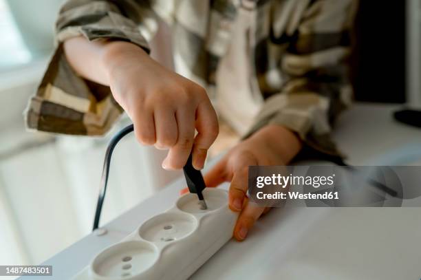boy plugging cable in socket at home - steckerleiste stock-fotos und bilder