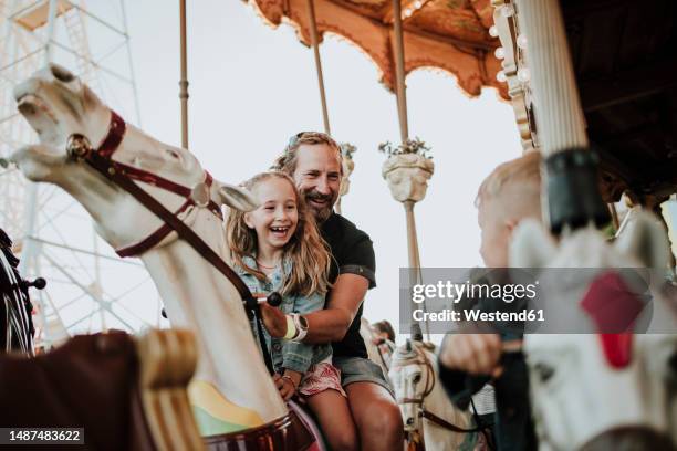 happy girl enjoying carousel ride with father at amusement park - parque de diversiones fotografías e imágenes de stock