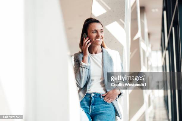 smiling businesswoman with hand in pocket talking on smart phone at office - hands in pockets stock pictures, royalty-free photos & images
