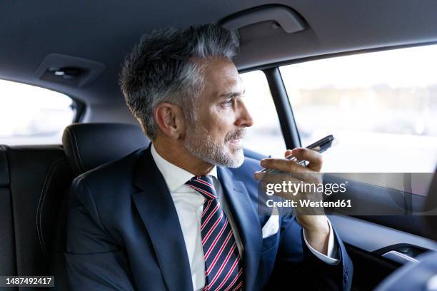 businessman talking on speaker phone sitting in car - speech recognition stockfoto's en -beelden