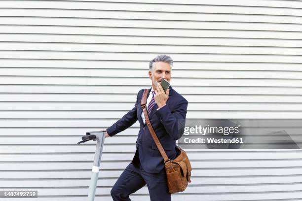 businessman with electric scooter talking on smart phone in front of wall - voice command stock pictures, royalty-free photos & images