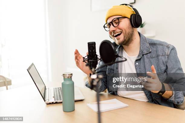 young smiling man recording podcast and doing live streaming using microphone and headphones in recording studio - commentator stockfoto's en -beelden