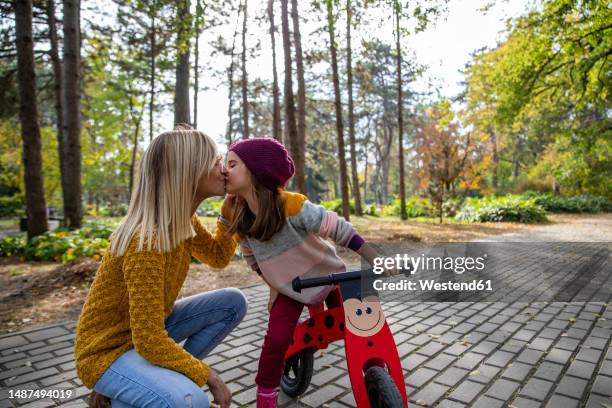 daughter with bicycle kissing mother on footpath at park - beso en la boca fotografías e imágenes de stock