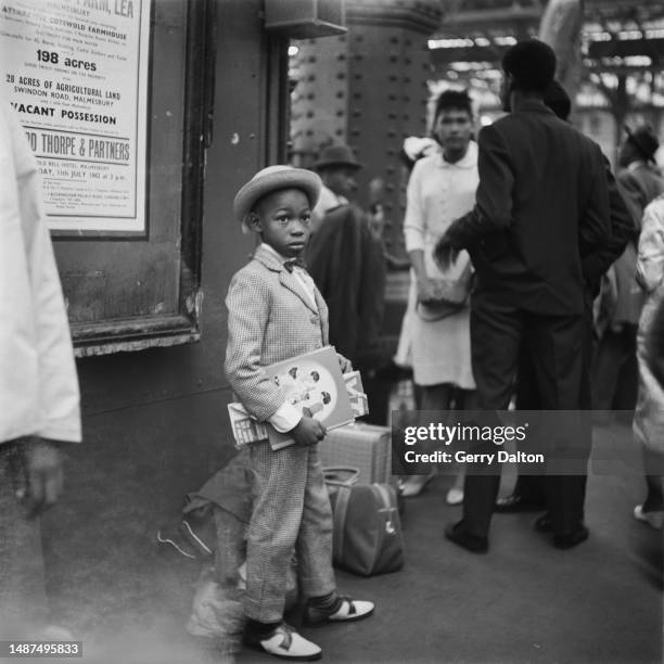 Boy wearing a hat, suit and bowtie, with books under his arm at Waterloo Station in London, England, 30th June 1962. The boy is among West Indians...