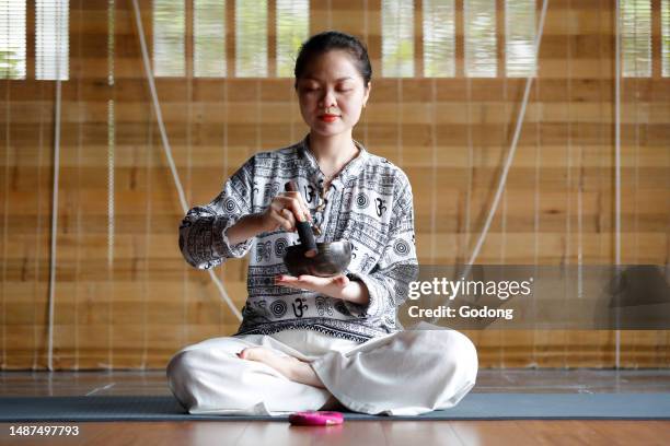 Buddhist woman holding and playing a tibetan singing bowl with a wooden stick. Tibetan bowl is used in sound therapy, meditation and yoga. Vietnam.
