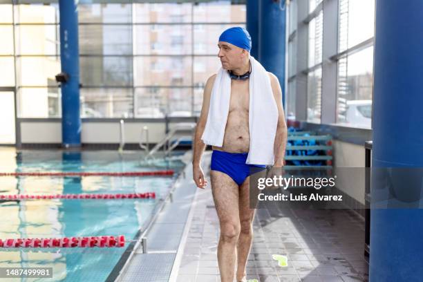 senior man walking at the poolside of a public swimming pool - zwembroek stockfoto's en -beelden