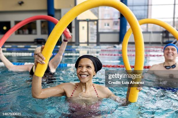 healthy senior woman doing swim noodle exercises in aerobics pool class - seniors exercising stock pictures, royalty-free photos & images