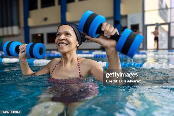 active senior woman workout in a swimming pool with aqua dumbbells - physiotherapie stock-fotos und bilder