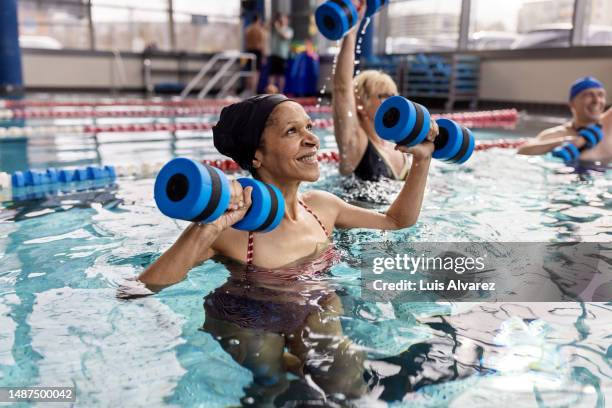 healthy senior woman exercising at aqua aerobics class in pool - senior swimming stock pictures, royalty-free photos & images