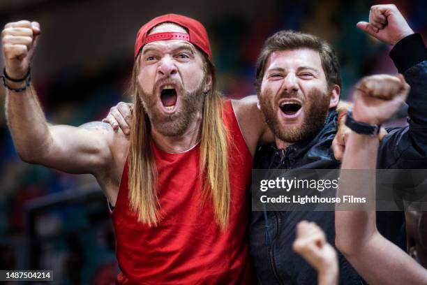 two thrilled male soccer fans yell passionately with their fists raised while standing in the stadium bleachers - gripping stock pictures, royalty-free photos & images