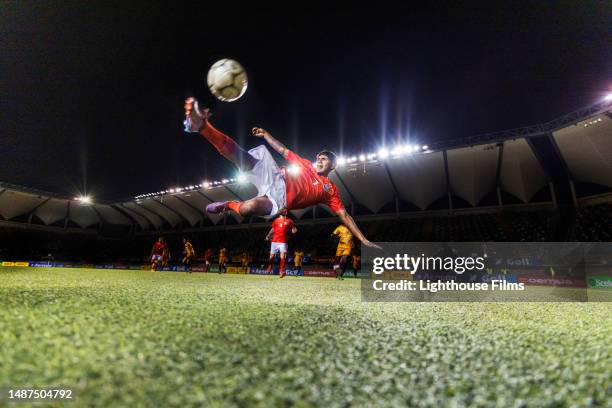 wide shot photo of male athlete impressively bicycle kicking a soccer ball while in mid-air - football strip imagens e fotografias de stock