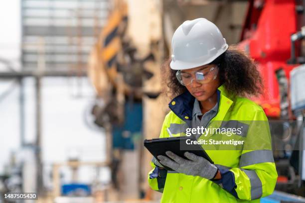 trabajando con un ambiente inteligente y seguro. una ingeniera africana trabaja en una fábrica y examina las instalaciones de maquinaria con una tableta digital. - seguridad y salud ocupacional fotografías e imágenes de stock