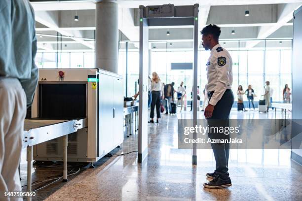 hispanic male airport security guard waiting for passengers to pass the metal detector machine - security pass stockfoto's en -beelden