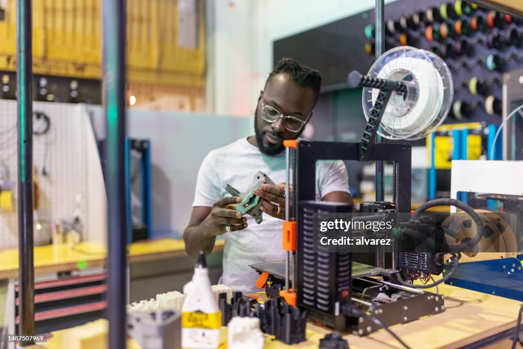 Young African man examining a 3d printed part at creative lab
