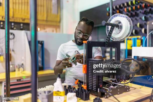 jovem africano examinando uma peça impressa em 3d no laboratório criativo - breaking new ground - fotografias e filmes do acervo